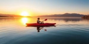 Kayaker paddling on a calm lake at sunrise.