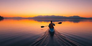 Kayaker paddles across calm water at sunset